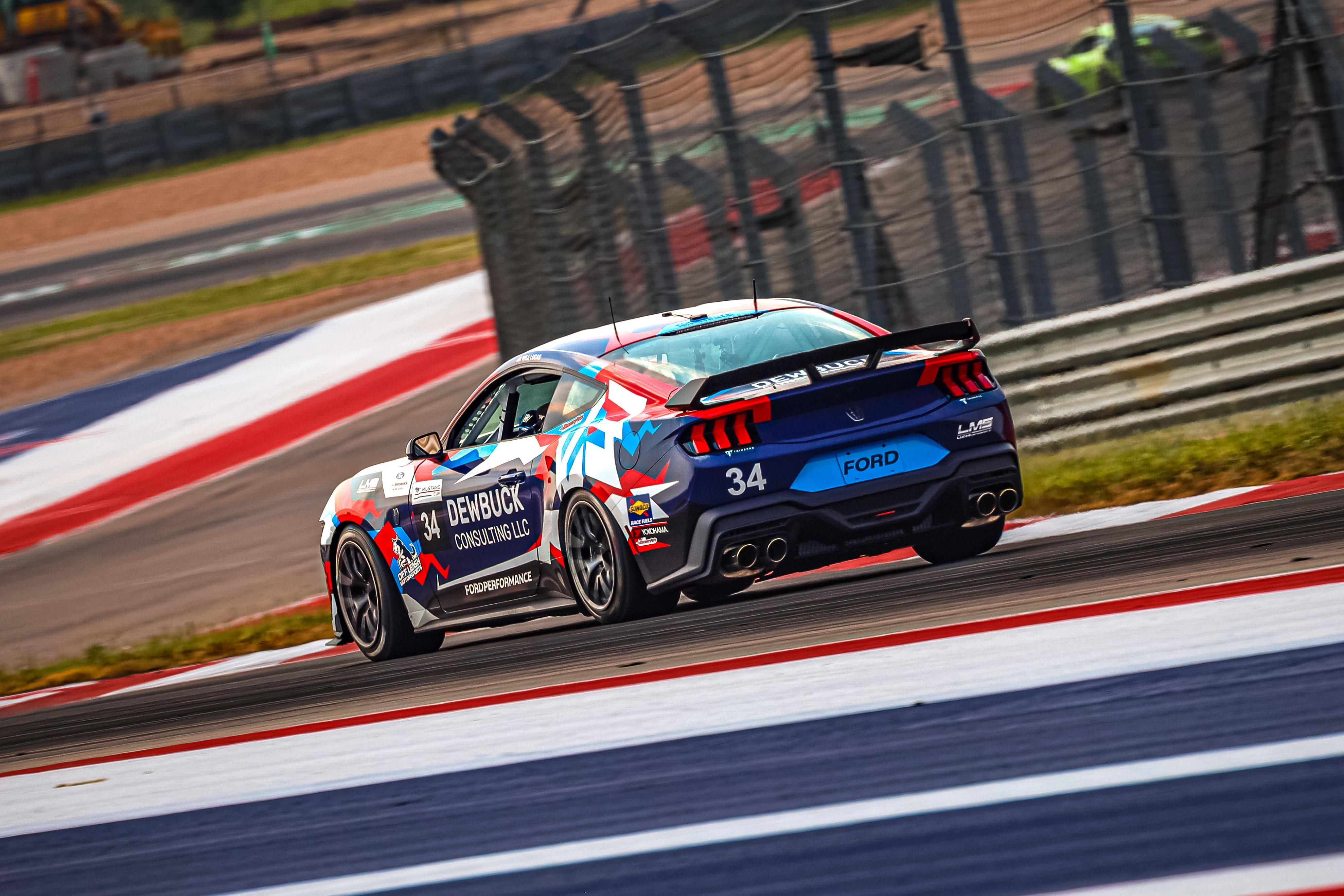 A red, white, and blue mustang races around a track.